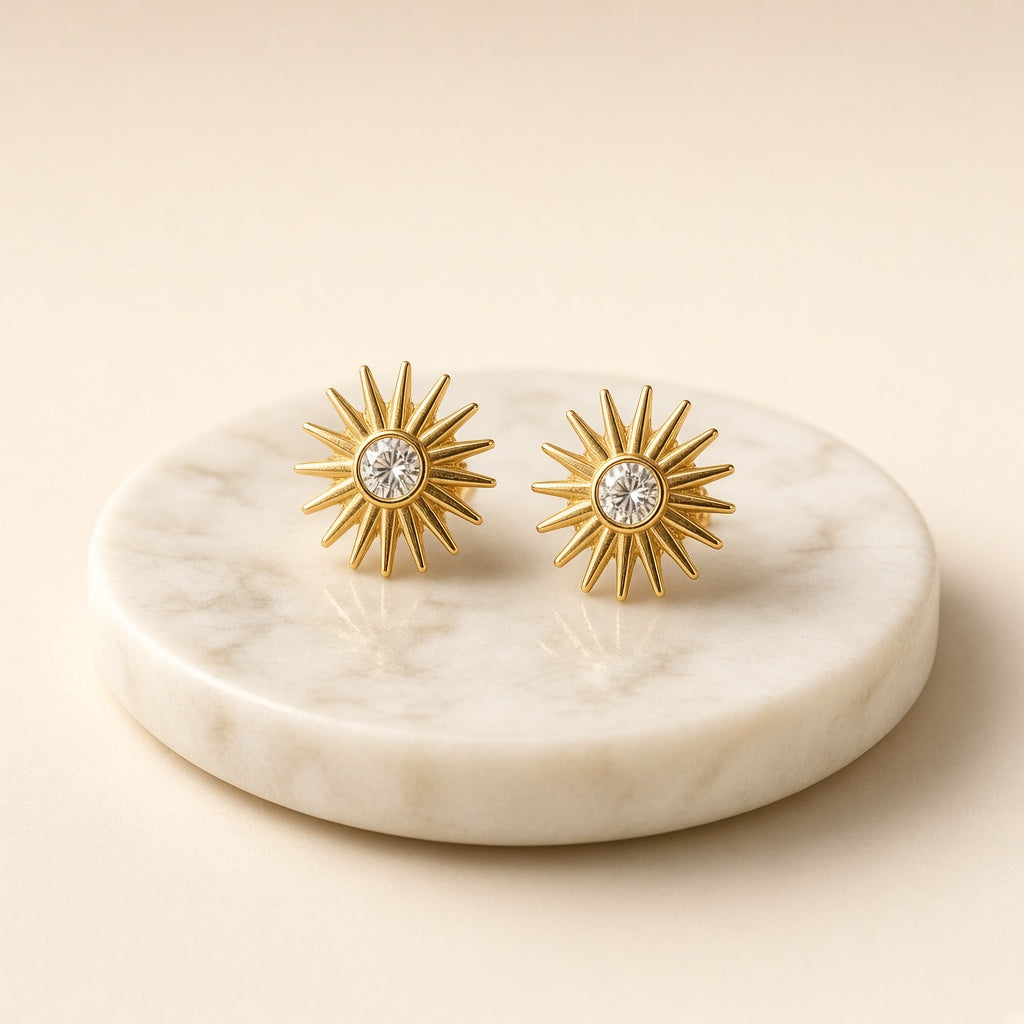 Gold sunburst stud earrings on a marble dish